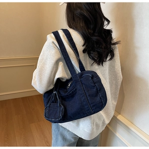Dettaglio borsa a tracolla in denim blu scuro con cuciture verticali e mini borsellino