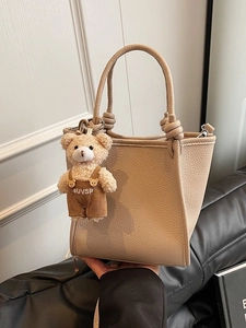 Beige lychee leather bucket bag with knotted handle and plush bear pendant detail