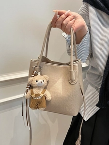 Chic beige lychee grain bucket bag with cute plush bear charm and adjustable strap