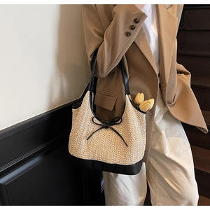 Detail of woven straw tote bag with black leather handles and delicate bow decoration