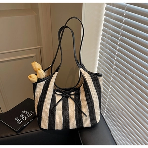 Detail of handwoven striped tote bag with black leather straps and decorative bow