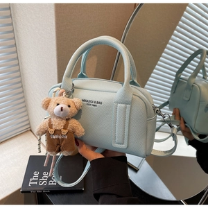 Detail of light blue pebble leather bag with zipper, handles and cute bear charm