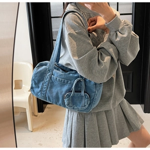 Dettaglio della borsa a cilindro in denim blu e portamonete coordinato indossati dal modello