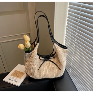 Detailed macro view of woven straw tote bag with black leather trim and bow on a sofa
