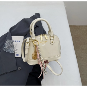 Close-up of a glossy beige shell handbag with gold zippers and tennis charm decoration