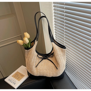 Detail of woven straw tote bag with black trim and elegant bow against soft shadows