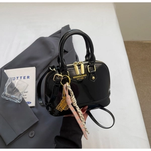 Close-up of black patent leather shell bag with gold hardware and birdcage charm