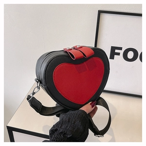 Detail of heart-shaped crossbody bag featuring black pebbled leather and red heart patch