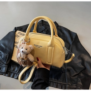 Detail of yellow lychee leather Boston bag with plush bear charm and printed text