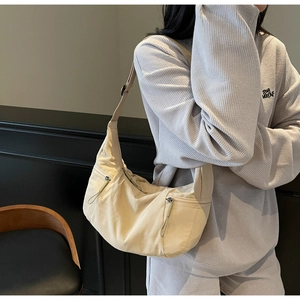 Detail of light yellow nylon crescent bag featuring two front zipper pockets and drawstring