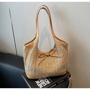 Detailed close-up of woven straw tote bag featuring a leather bow and brown strap