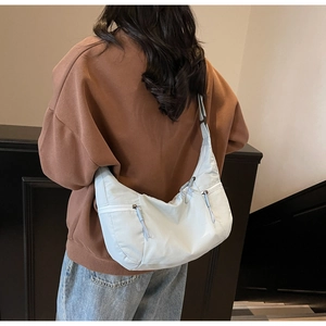Detail view of light blue crescent bag with front zipper pockets worn by a person