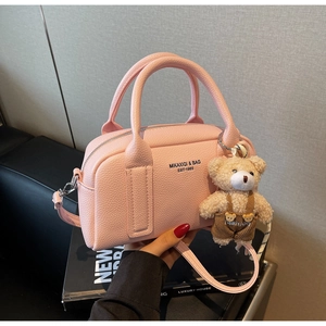 Pink litchi texture Boston bag detail with brand text and cute bear plush pendant