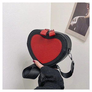 Detail view of heart-shaped crossbody bag with red contrast patch and wide nylon strap