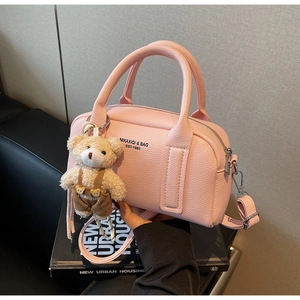 Detail of pink lychee leather handbag with brand logo and cute brown teddy bear charm