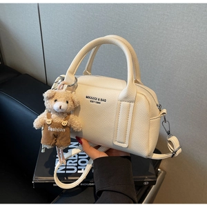 Detail of cream pebbled leather bowling bag featuring a plush bear charm and sturdy handles