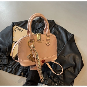 Pink shell handbag detail with golden hardware and decorative keychain on dark backdrop