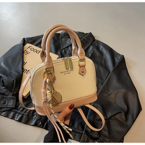 Detailed close-up of a beige shell-shaped handbag with tennis racket charm and tassel