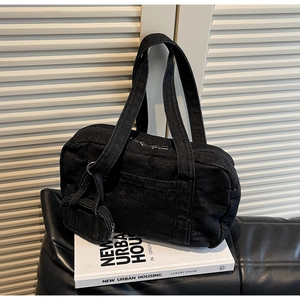 Dettaglio borsa a spalla in denim nero con mini portamonete su libro bianco e sfondo in pelle