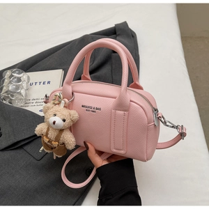 Detail view of pink litchi grain leather bowling bag with cute teddy bear charm