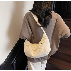 Detail view of cream crescent bag featuring dual front zip pockets and adjustable wide strap