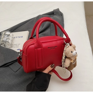 Close-up of red litchi grain bowling bag with a cute plush bear charm and long strap