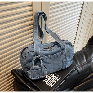 Dettaglio della borsa a cilindro in denim blu con mini pochette su divano in pelle nera