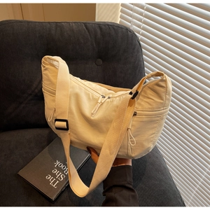 Detail of a creamy nylon crescent bag with adjustable straps on a stylish grey sofa