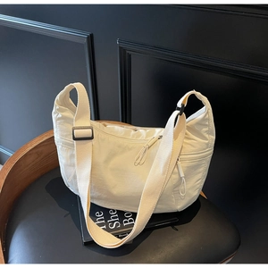 Close-up of cream nylon crescent bag with adjustable wide strap on a black chair