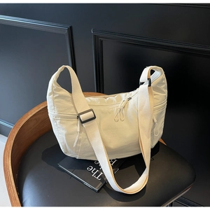 Detail of off-white nylon crescent bag with adjustable strap on a leather chair