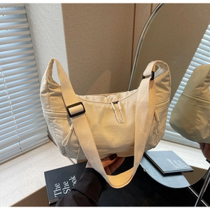 Close-up of ivory nylon crescent bag with adjustable wide strap and front zipper pocket