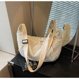 Detail of off-white nylon crescent bag showing adjustable strap and zipper pockets