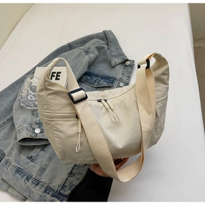 Detailed view of cream-colored nylon crescent bag with adjustable wide strap and dual zippers