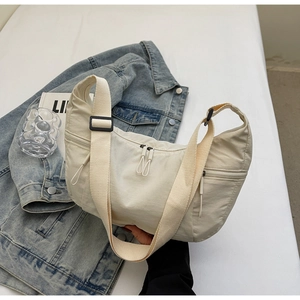 Detail of a beige crescent crossbody bag with adjustable wide strap and metal zippers
