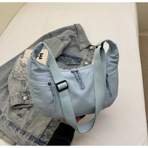 Close-up of light blue nylon crescent bag with multiple pockets on denim jacket background
