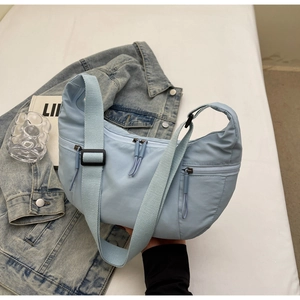 Close-up of light blue crescent nylon bag featuring multi-zipper compartments and wide strap