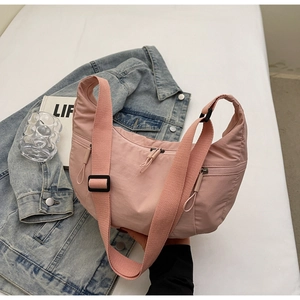 Detail of pink crescent bag showing adjustable strap and front zipper pocket in a casual setting