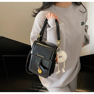 Detail of black vintage faux leather crossbody bag with gold lock and plush charm