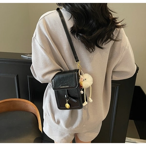 Detail of black leather crossbody bag with fashion text and white plush charm on model
