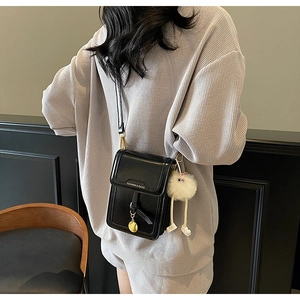 Detail of black leather crossbody phone bag with gold charm and plush doll pendant