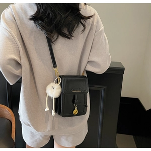 Close-up of black leather mobile bag with gold hardware and white plush doll charm