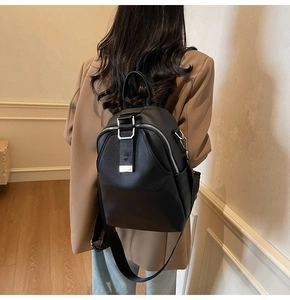Detail of black pebbled leather backpack with silver zippers on a model in a brown blazer
