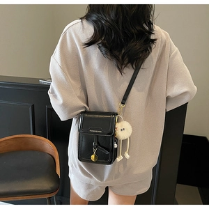 Detailed back view of a black leather mini crossbody bag with a white plush charm