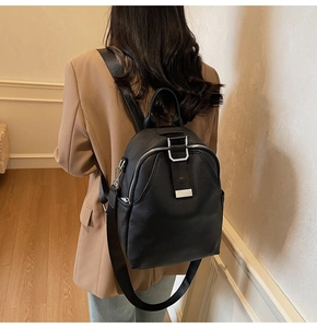 Rear view of black leather backpack with pebble grain texture on female model in a blazer