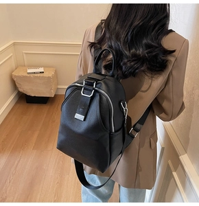 Detail of black pebbled leather backpack showing silver zippers and wide fabric straps