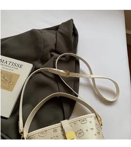 Detail of adjustable long shoulder strap and golden metal buckle on cream PU bucket bag