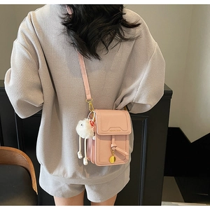 Close-up of pink crossbody phone bag with adjustable strap and plush ball charm detail