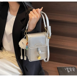 Detail of silver metallic rectangular bag with plush ball charm on wooden stairs