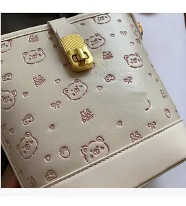 Detailed view of white leather bag featuring cartoon bear embossing and gold lock hardware
