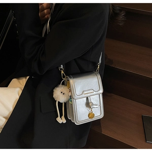 Silver metallic crossbody bag with white plush monster charm on dark wood stairs background